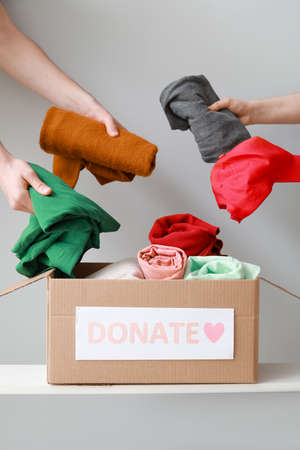 Women putting donation clothes in box on shelf against light backgroundの写真素材