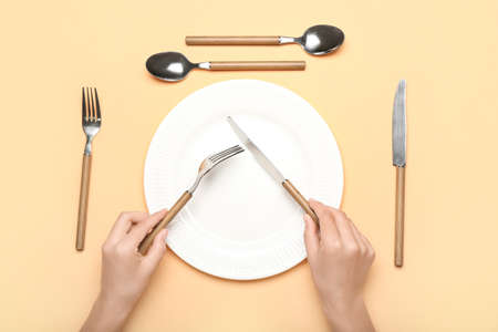 Woman with set of cutlery and plate on color background