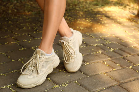 Legs of woman in white sneakers on pavement, closeup