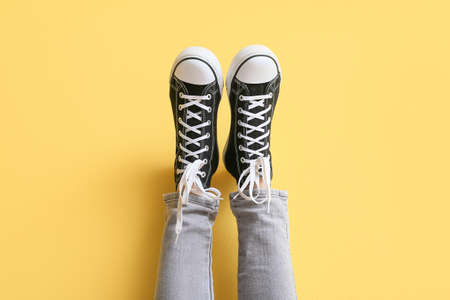 Legs of woman in black sneakers with white laces on yellow background