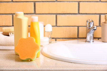 Bath sponge and bottles of cosmetic products on table near sinkの写真素材