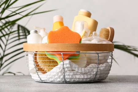 Basket with different bath accessories and cosmetics on table near light wallの写真素材