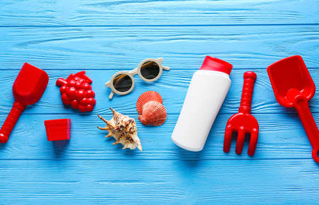 Set of beach accessories for children and bottle of sunscreen on color wooden background