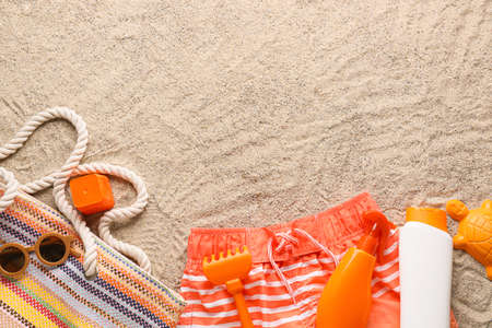 Set of beach accessories for children, swimsuit and bottles of sunscreen on sand, closeup