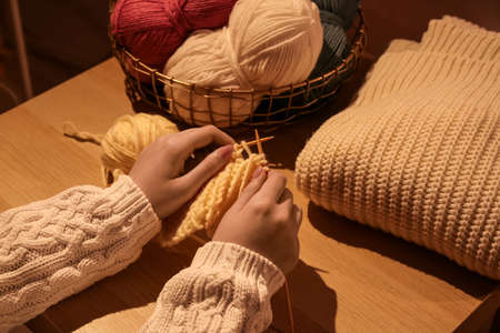 Young woman knitting clothes on wooden background