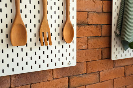 Peg board with wooden spatulas hanging on brick wallの写真素材