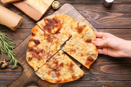 Woman eating tasty khachapuri on wooden background