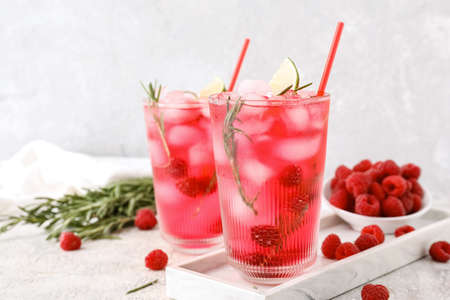 Glasses of tasty raspberry lemonade and berries on light background