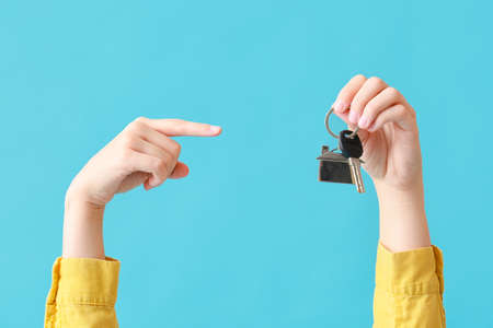 Young woman pointing at key from house on blue background
