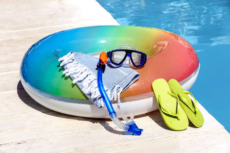 Inflatable ring, towel, flip-flops, snorkeling mask and tube on edge of swimming pool