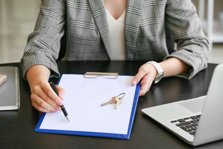 Real estate agent with clipboard and key from house in office, closeup