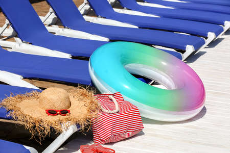 Stylish hat, sunglasses, bag and inflatable ring on edge of swimming pool