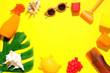 Frame made of beach accessories for children and bottles of sunscreen on color background