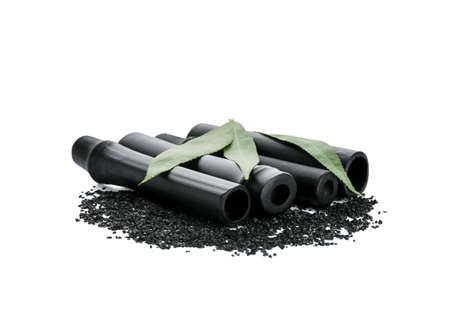 Composition with black bamboo sticks, activated carbon powder and leaves on white background