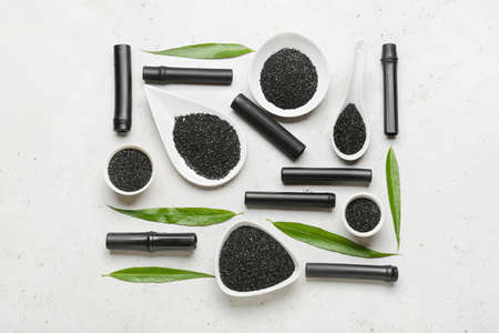 Composition with bowls of activated carbon powder, bamboo sticks and leaves on light background