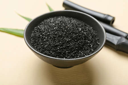 Bowl of activated carbon powder on color background, closeup