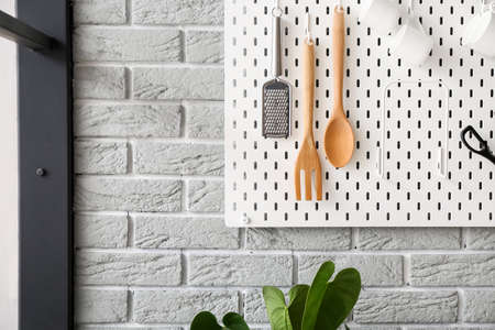 Pegboard with kitchen utensils and cups on gray brick wallの写真素材