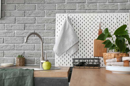 Modern counter and pegboard with kitchen utensils near gray brick wallの写真素材