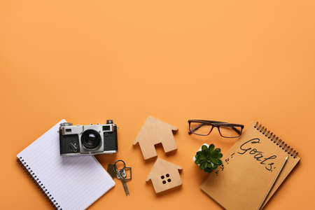 Notebook with to do list, photo camera and models of house on color background. new year goals