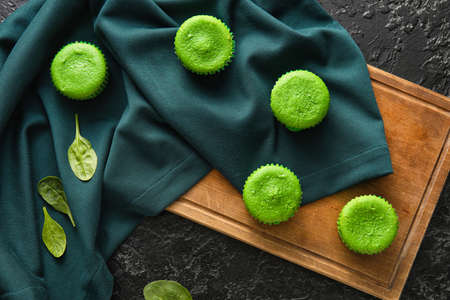 Wooden board with tasty spinach muffins on dark backgroundの写真素材