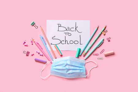 Paper with text BACK TO SCHOOL, stationery and medical mask on color backgroundの写真素材