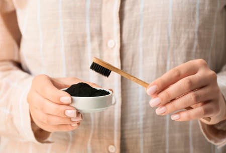 Woman holding bowl with activated charcoal tooth powder and brush, closeupの写真素材