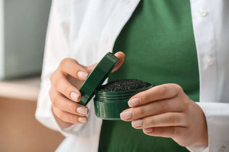 Woman holding jar with activated charcoal tooth powder indoors, closeupの写真素材