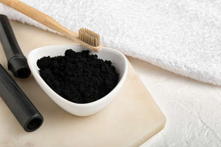 Bowl with activated charcoal tooth powder, brush and bamboo sticks on white backgroundの写真素材