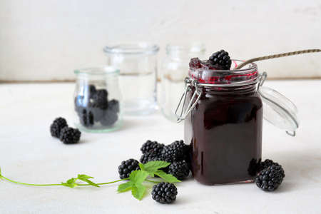 Jar of tasty blackberry jam and berries on light backgroundの写真素材