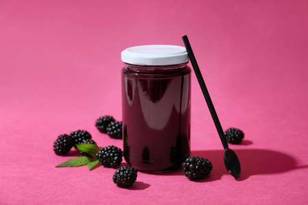 Jar of tasty blackberry jam and berries on color background