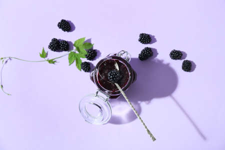 Jar of tasty blackberry jam and berries on color backgroundの写真素材