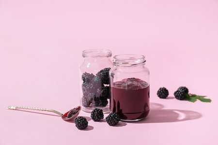 Jars with tasty blackberry jam and berries on color background