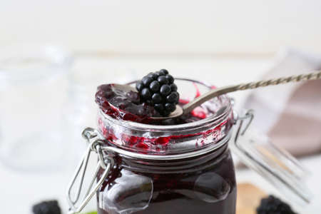 Jar and spoon with tasty blackberry jam on light background, closeupの写真素材
