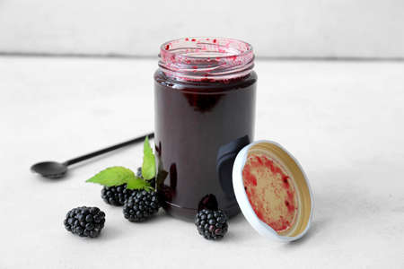 Jar of tasty blackberry jam and berries on light backgroundの写真素材