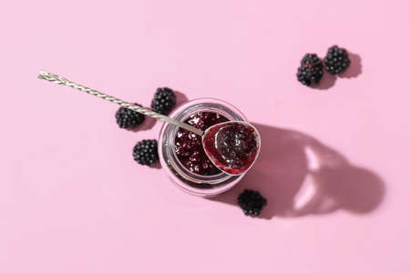 Jar and spoon with tasty blackberry jam on color backgroundの写真素材