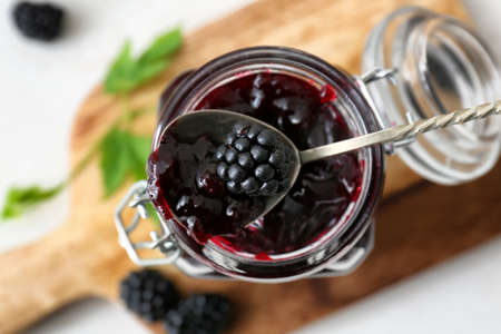Jar and spoon with tasty blackberry jam on light background, closeupの写真素材