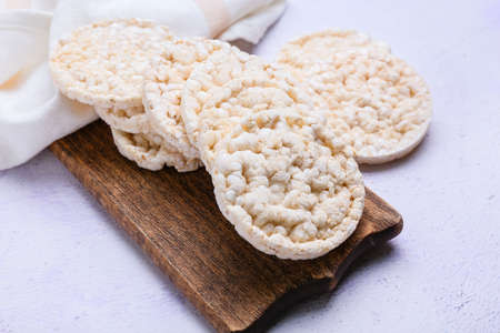 Board with crispy rice crackers on light background, closeup
