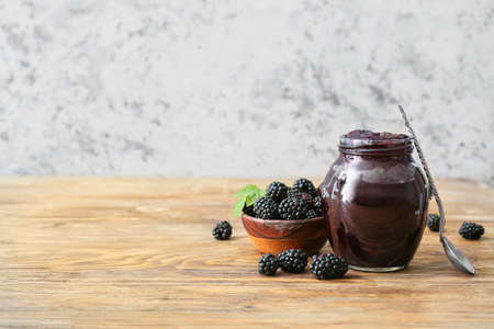 Jar of tasty blackberry jam and berries on wooden tableの写真素材