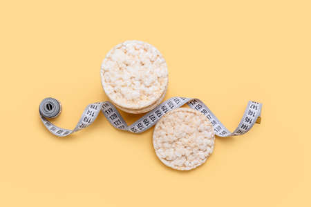 Rice crackers and measuring tape on color background