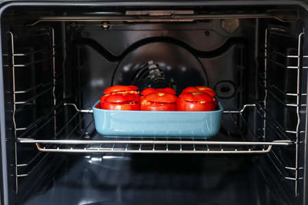 Baking dish with uncooked stuffed tomatoes in the oven