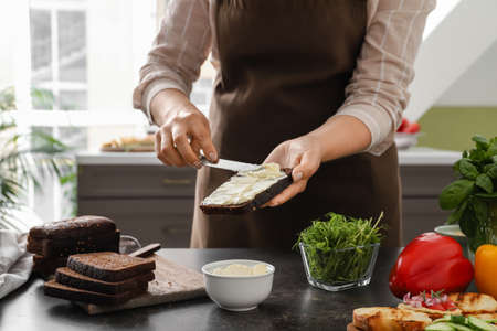 Woman spreading toast with dip at table in kitchenの写真素材