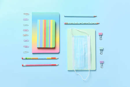 Set of stationery and medical mask on color background