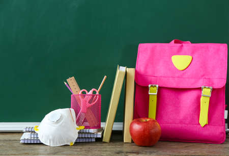 Set of stationery, backpack and respirator on table in classroomの写真素材