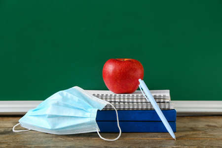 Books, apple and medical mask on table in classroom
