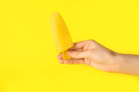 Female hand with tasty pineapple ice cream on color background