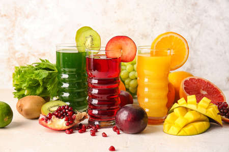 Glasses with healthy juice, fruits and vegetables on light backgroundの写真素材