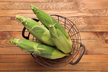 Basket with fresh corn cobs on wooden background