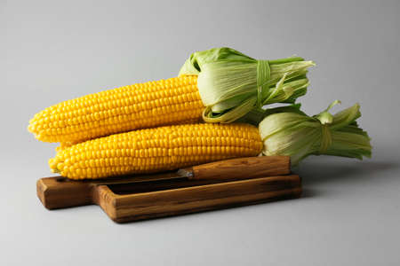 Wooden board with fresh corn cobs on light background