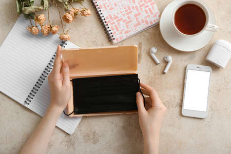 Female hands with medical mask case, mobile phone, earphones and cup of tea on table