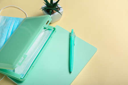 Medical masks with case, notebook and houseplant on color background, closeup